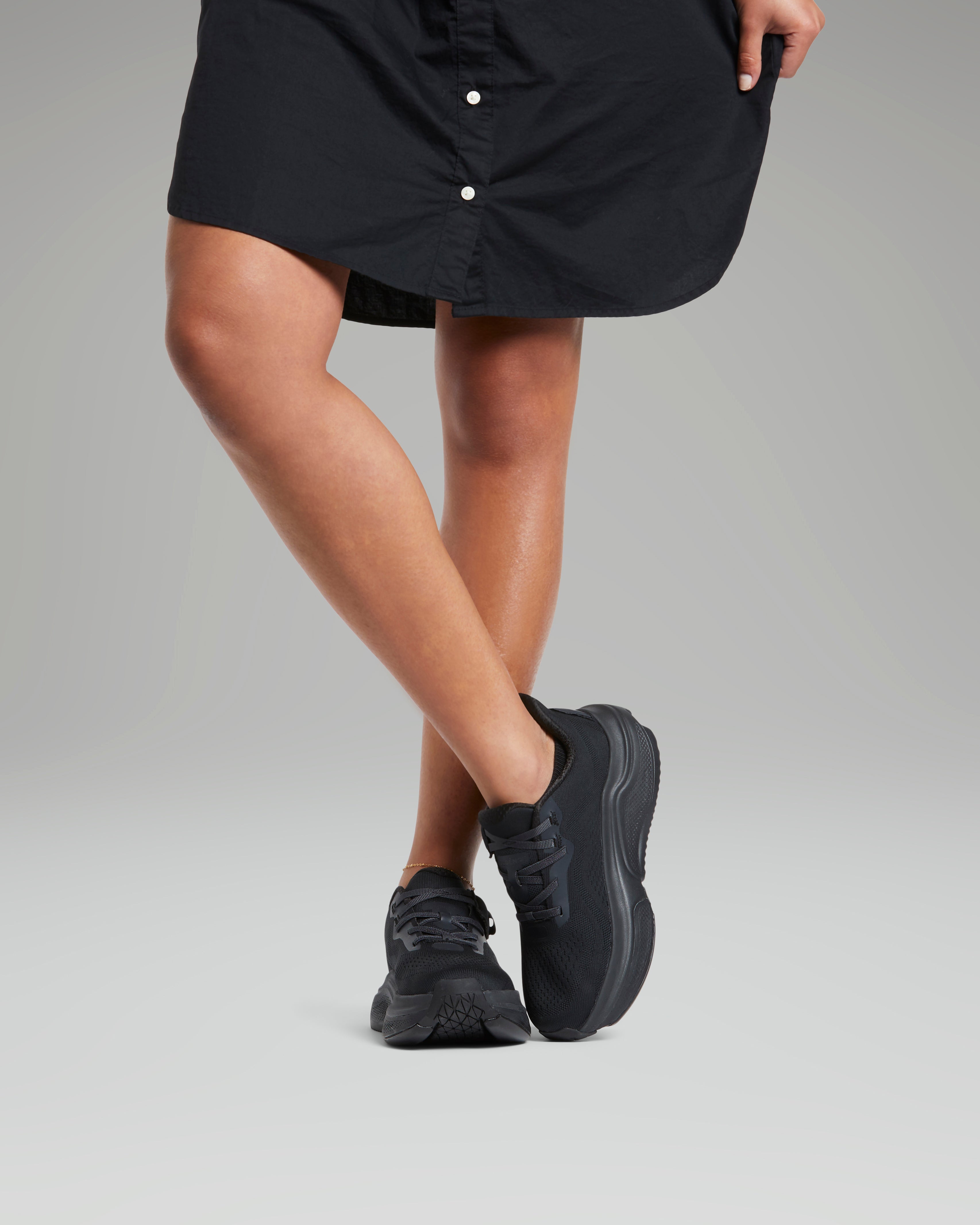 Person wearing black sneakers and a black skirt on a gray background