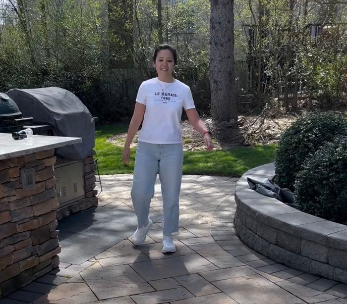 Person standing on a patio in a backyard with outdoor furniture and greenery.