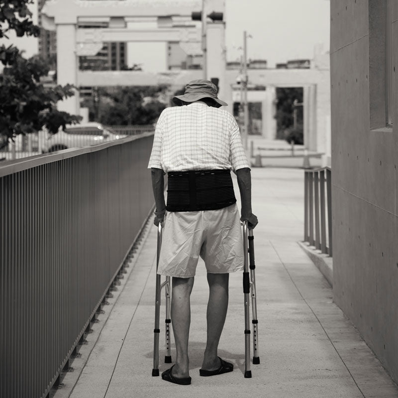 Person using crutches walking on a bridge with buildings in the background