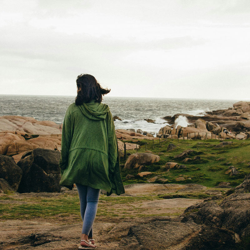 Person wearing a green jacket standing on rocky terrain by the ocean
