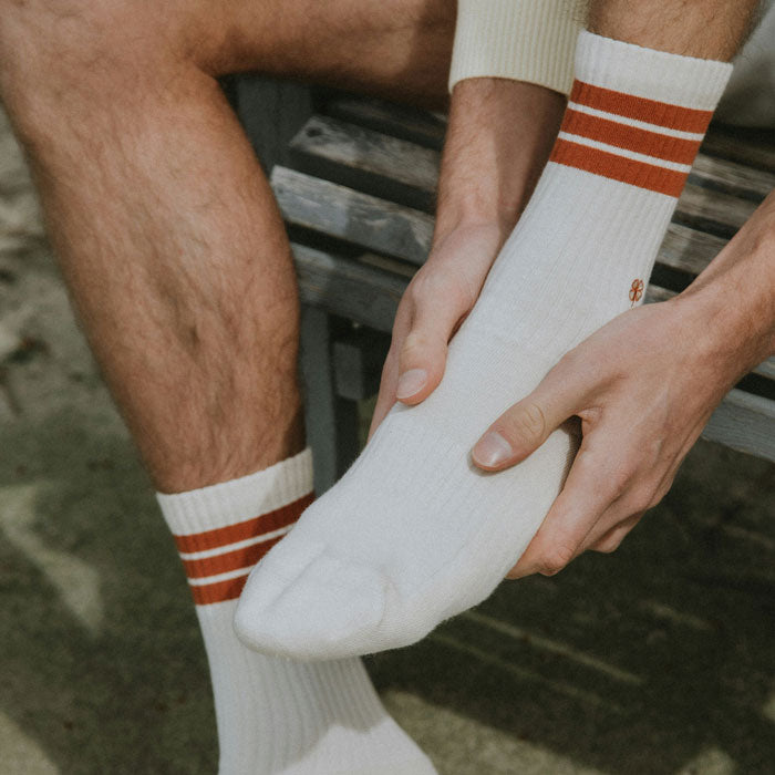 Person wearing white socks with red stripes, adjusting one on a bench.