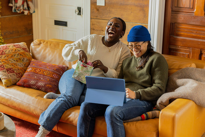Two people sitting on a couch with a laptop, laughing and interacting.
