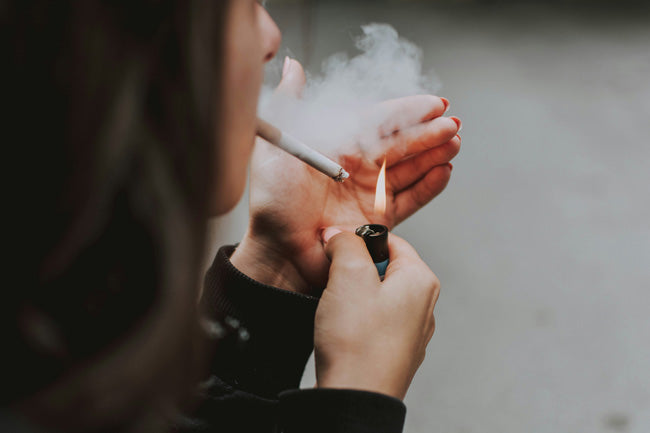 Person lighting a cigarette with a lighter, with smoke visible.