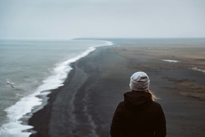 Person standing on a black sand beach looking at the ocean