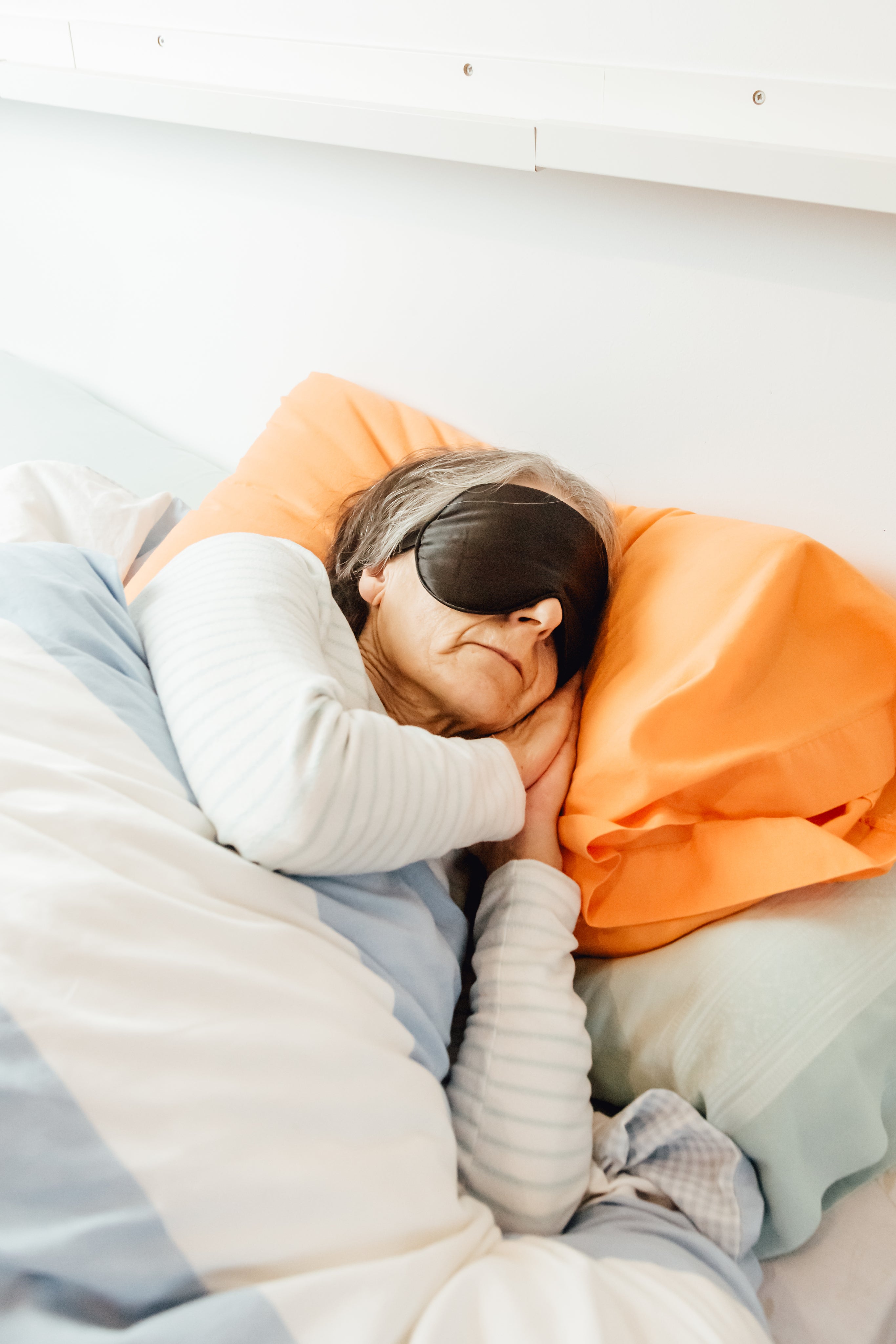 Person lying in bed with orange pillow and light blue blanket
