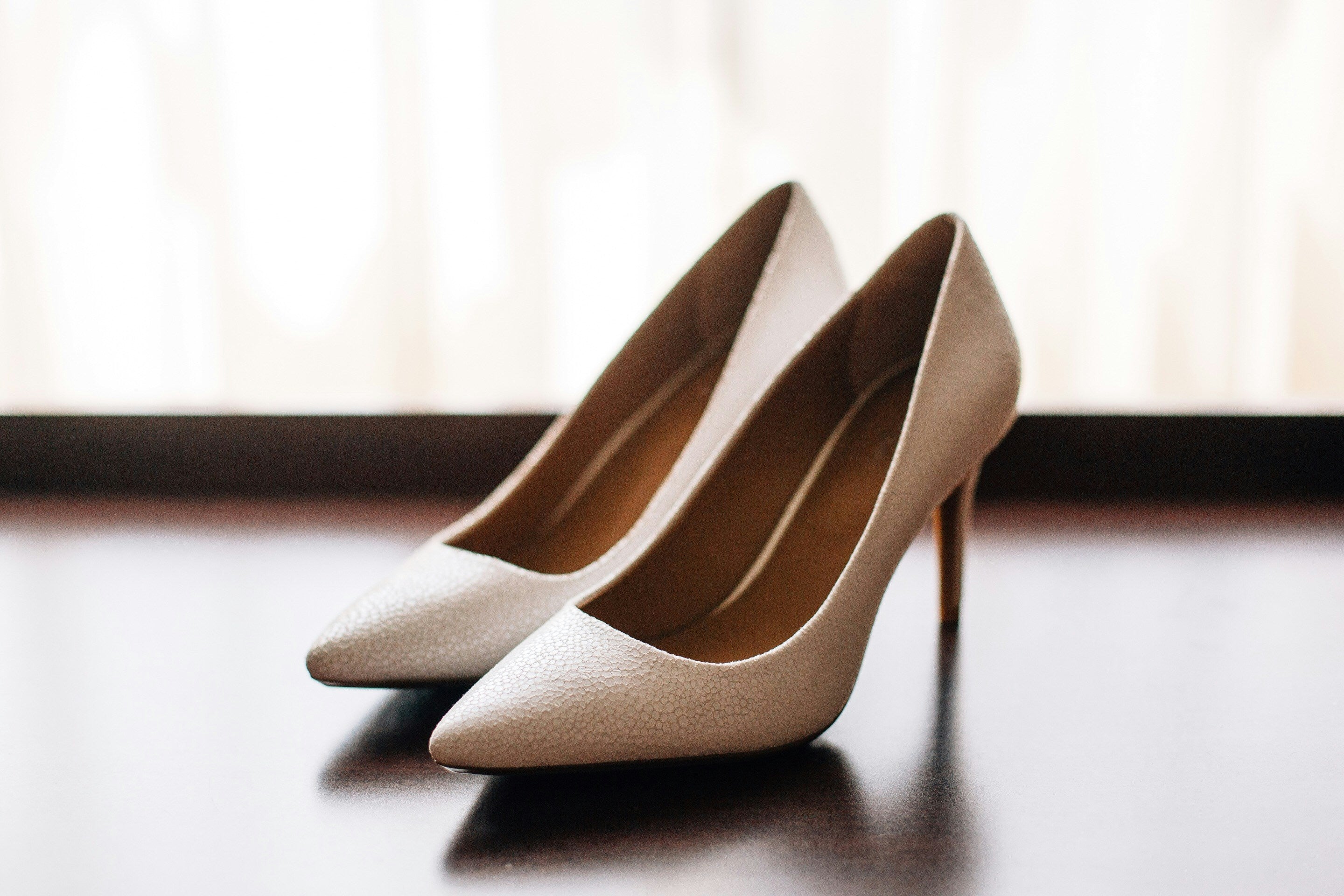 Pair of beige high-heeled shoes on a reflective surface with a blurred background