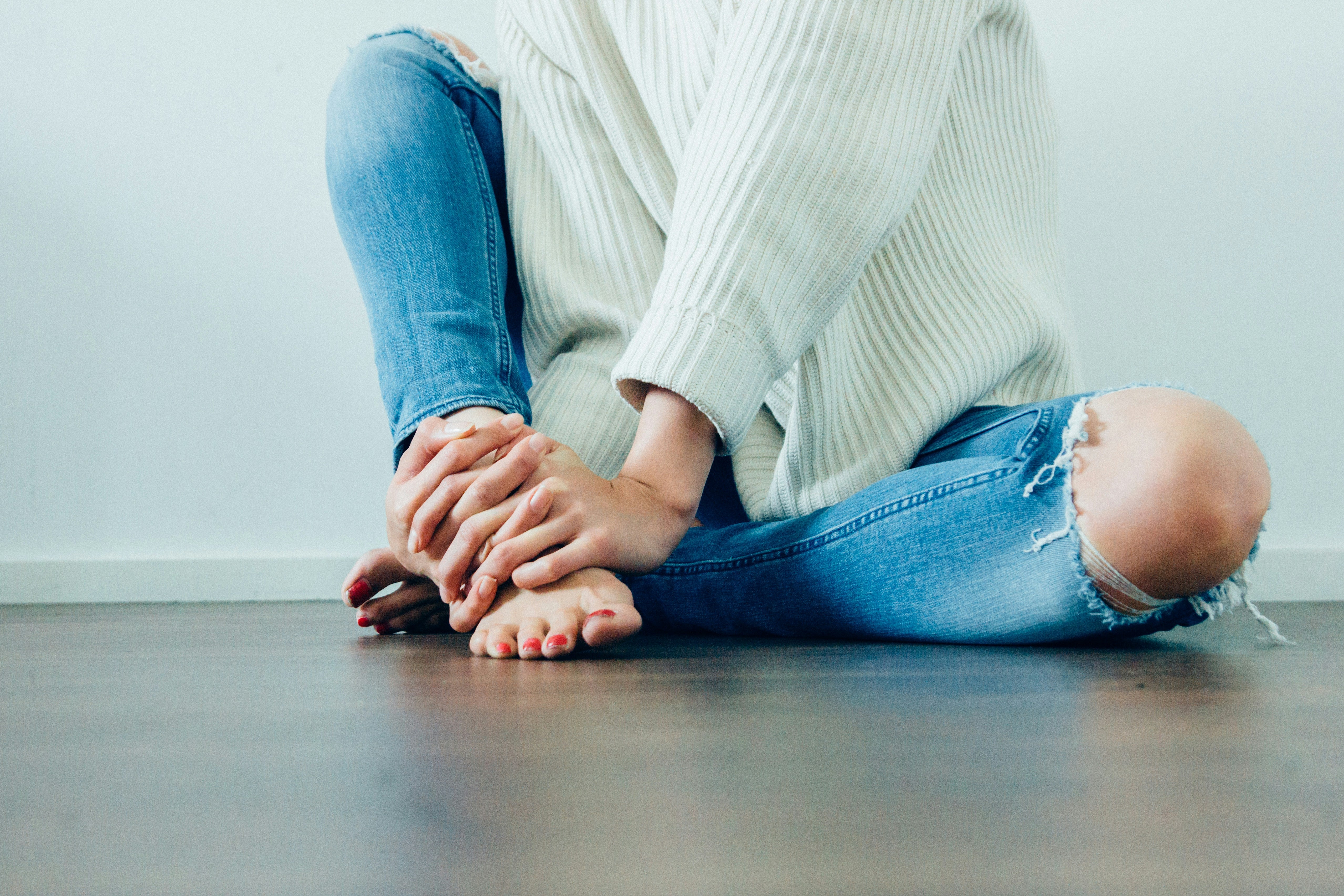 Person sitting on a floor wearing ripped jeans and a light sweater.