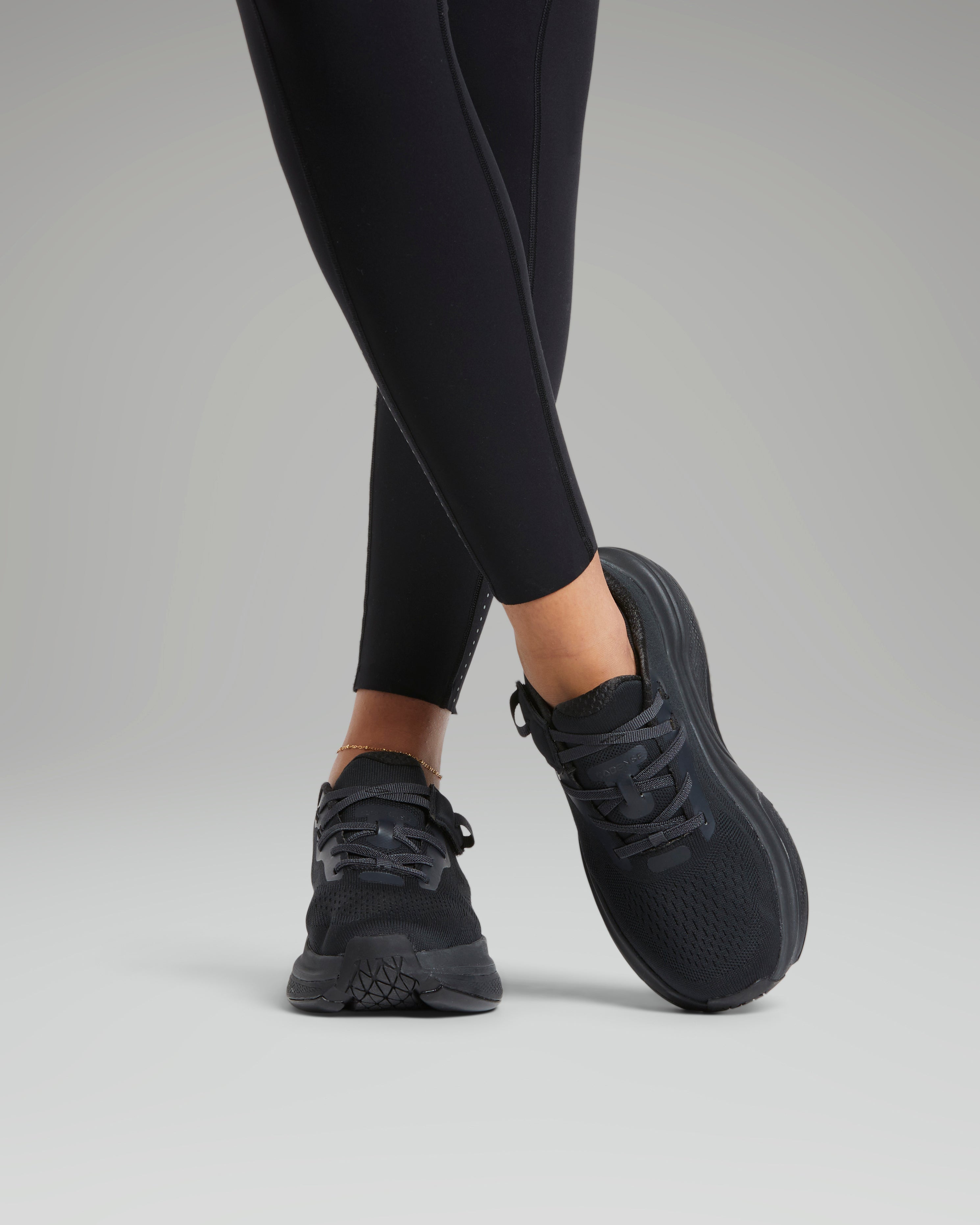 Black athletic shoes worn with black leggings on a gray background