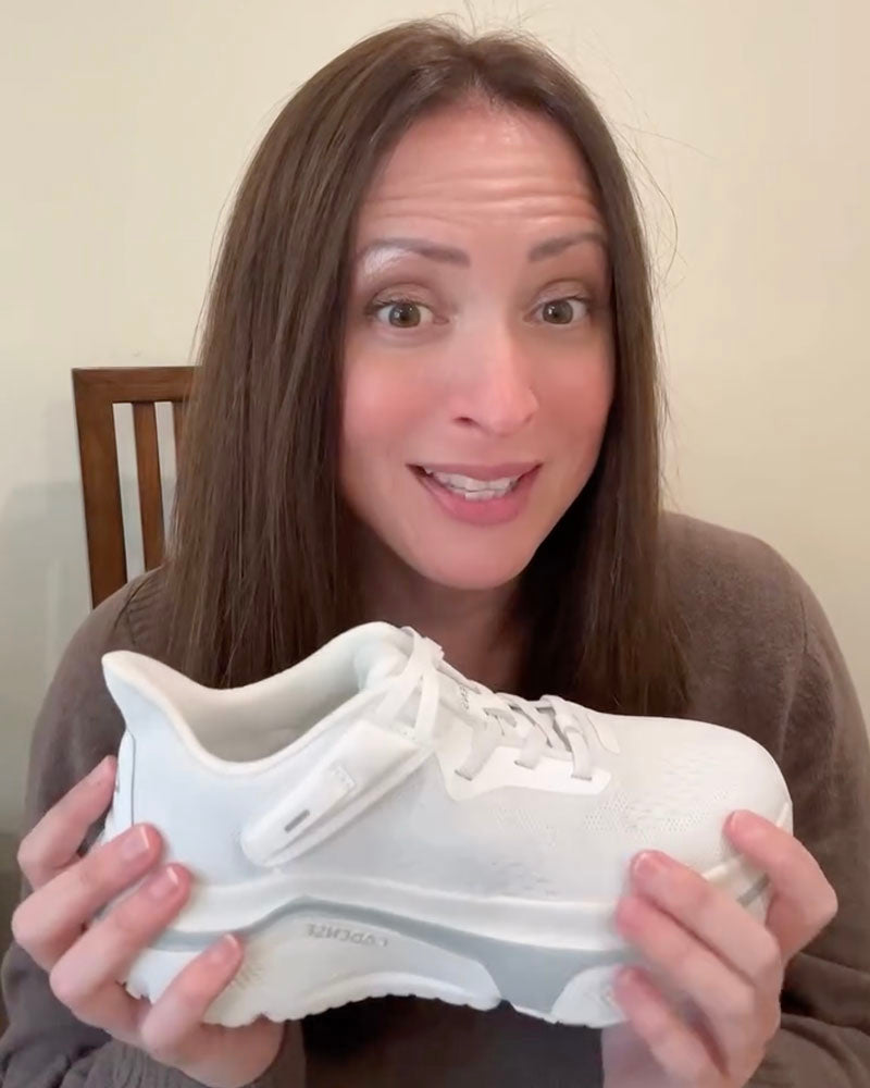 Woman holding a white sneaker against a neutral background