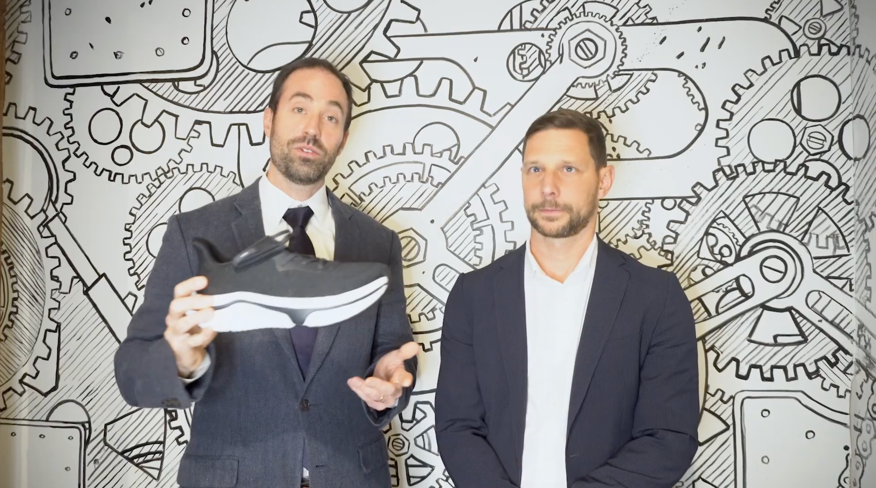 Two men in suits standing in front of a mechanical gear background