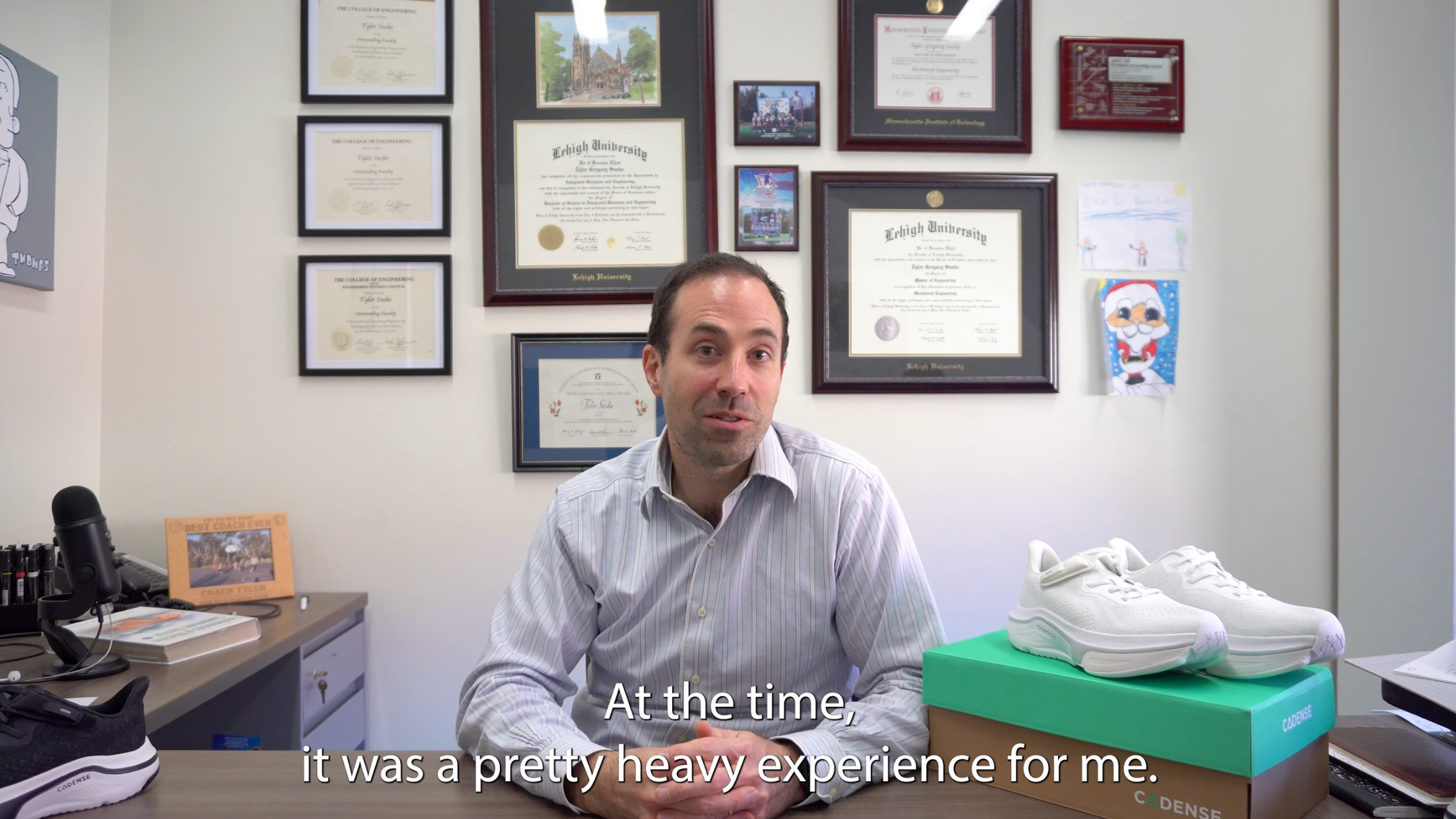 Man sitting at a desk with framed certificates on the wall and shoes on the desk