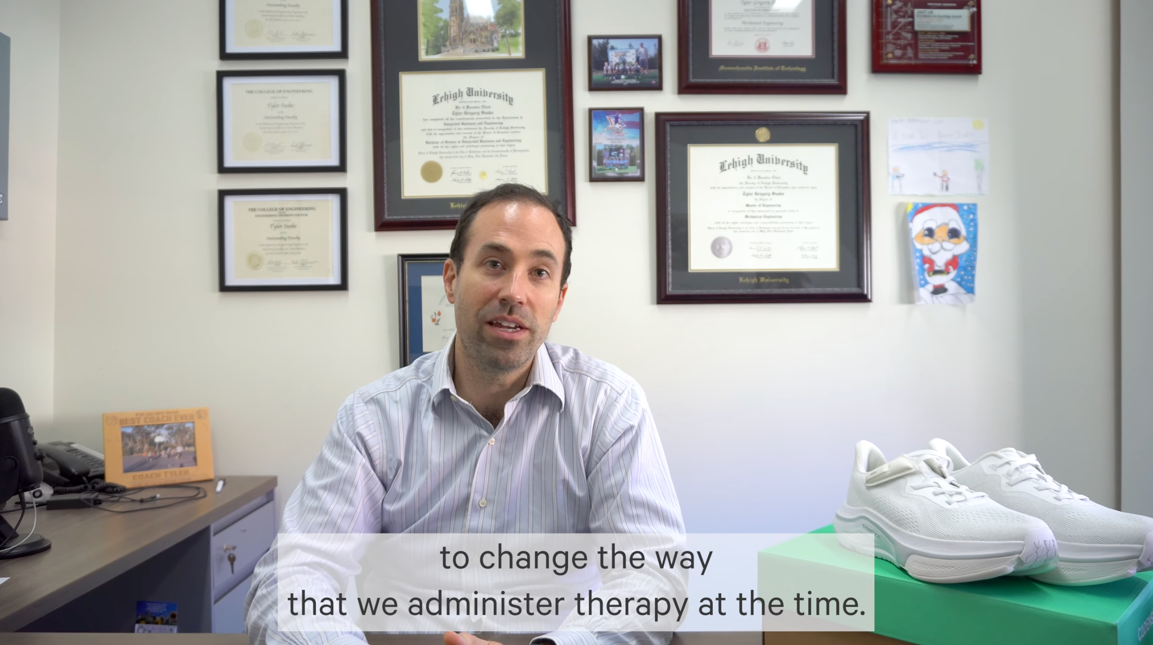 Man sitting at a desk with framed certificates on the wall behind him