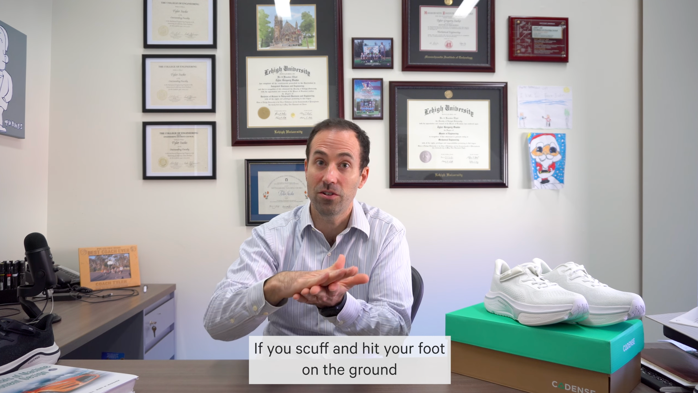 Man sitting at a desk with framed certificates on the wall, holding a white sneaker.