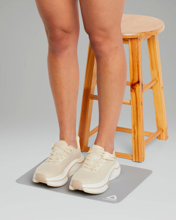 Person wearing beige sneakers on a gray mat with a wooden stool in the background